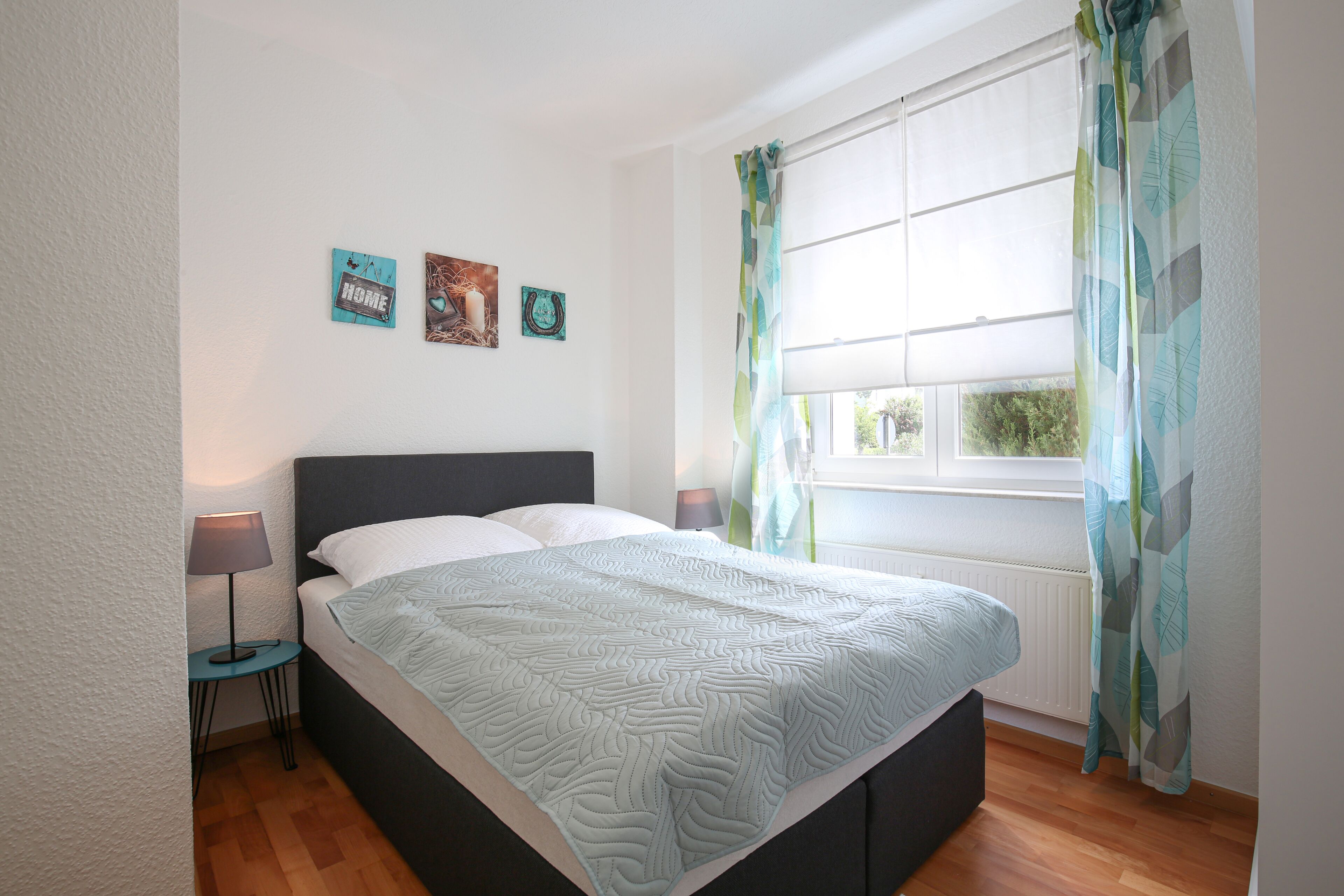 A bedroom with a bed, a nightstand, a window with curtains, and wall art.