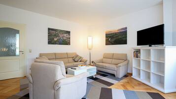 Ein Wohnzimmer mit zwei Sofas, einem Couchtisch, einem Fernseher und einem Bücherregal.