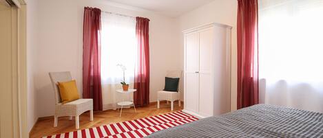 A bedroom with a bed, two chairs, a wardrobe, and a red and white striped rug.