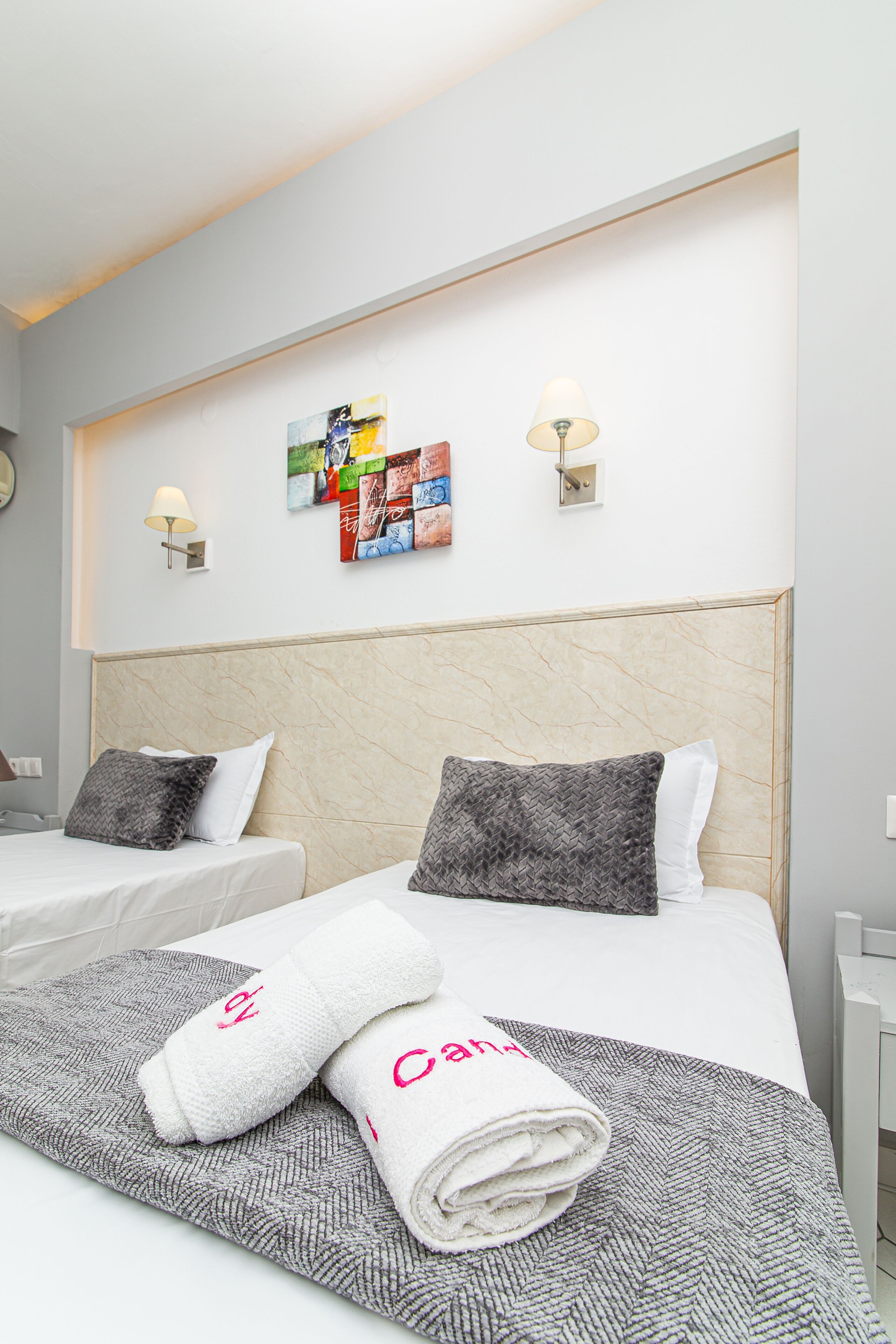 Habitación de hotel con dos camas, cabeceros, lámparas de pared y una obra de arte en la pared.