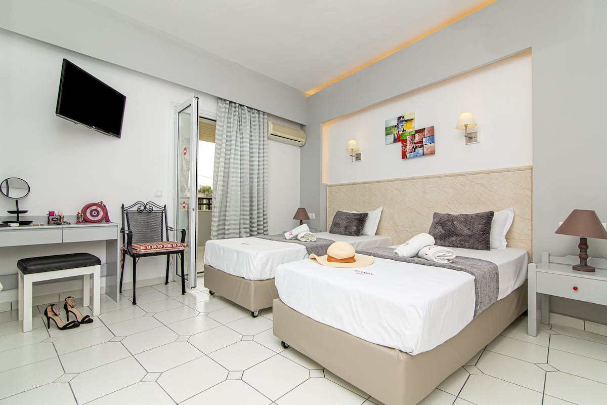 A hotel room with two beds, a desk, a chair, a TV, and a window with curtains.