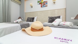 A hotel room with two beds, a large hat on the bed, and a wall with a colorful artwork. - ICandy Sol (Hersonissos)