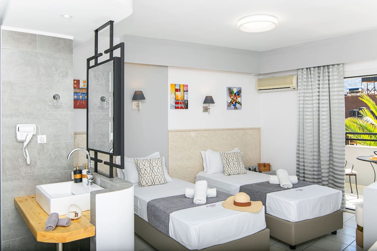 A hotel room with two beds, a bathroom with a sink, and a balcony with a view.