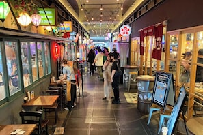 A narrow indoor corridor with multiple dining establishments, tables, and chairs.