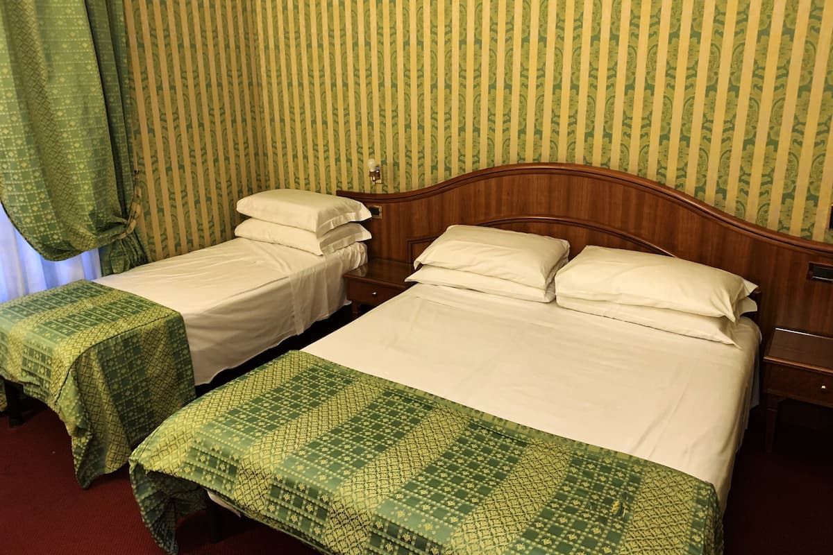 A hotel room with two beds, each with a green patterned bedspread and white linens.