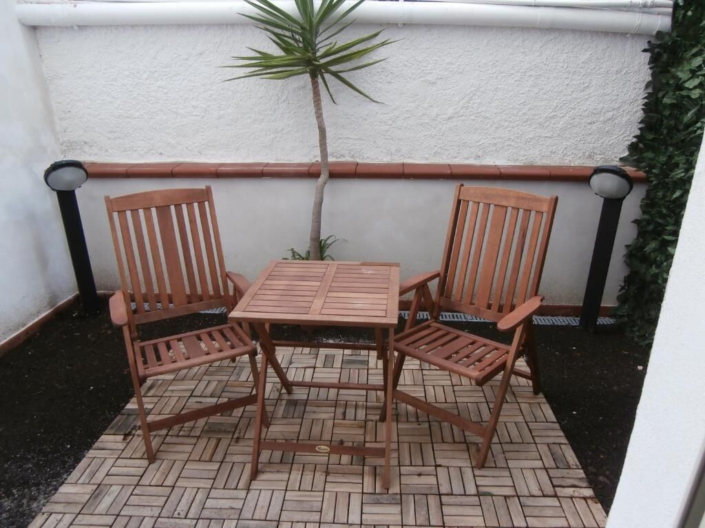 A small patio area with a wooden table and two chairs, surrounded by a white wall and a black railing.