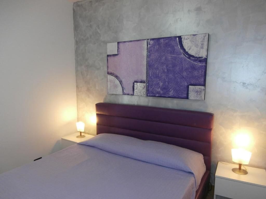 Ein Schlafzimmer mit einem Bett, zwei Nachttischen und einem an der Wand befestigten abstrakten Kunstwerk.
