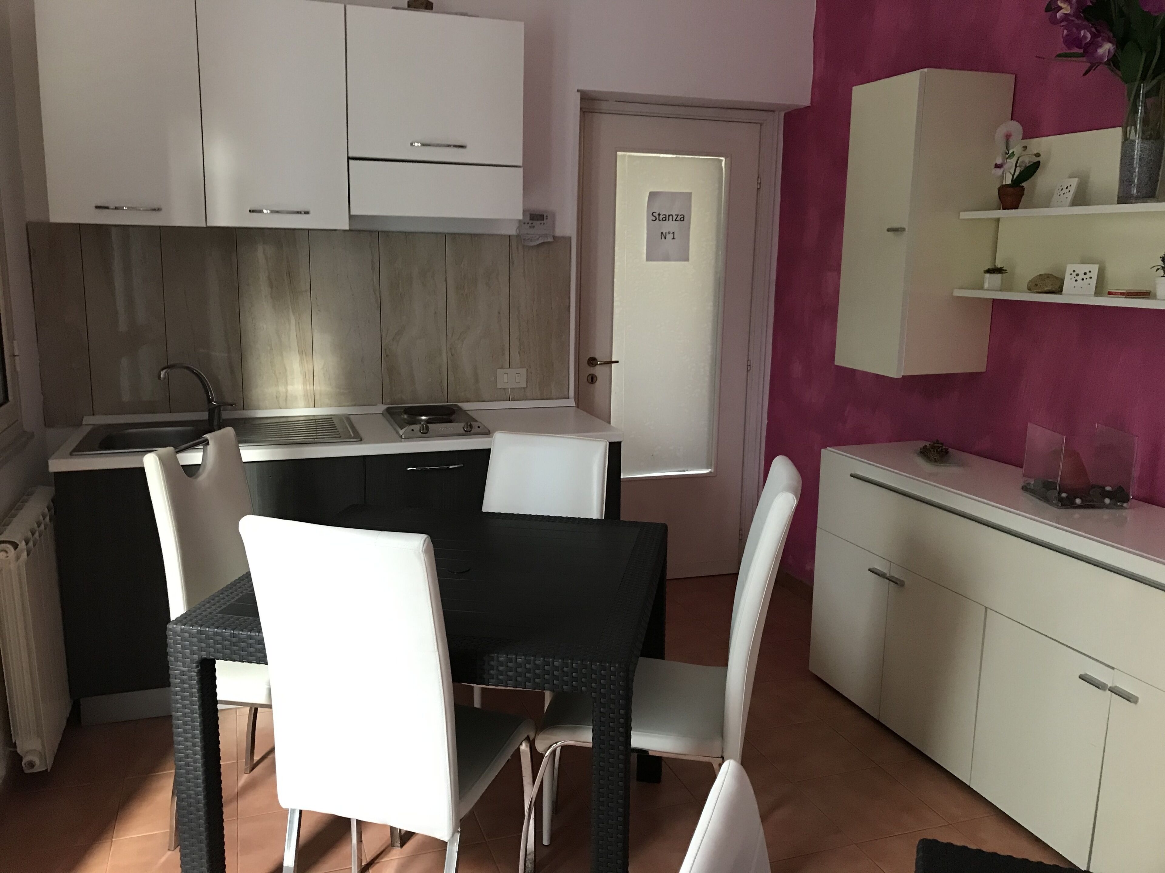 A compact kitchen with white cabinets, a black dining table, and white chairs. There's a small island with a sink and a stove.