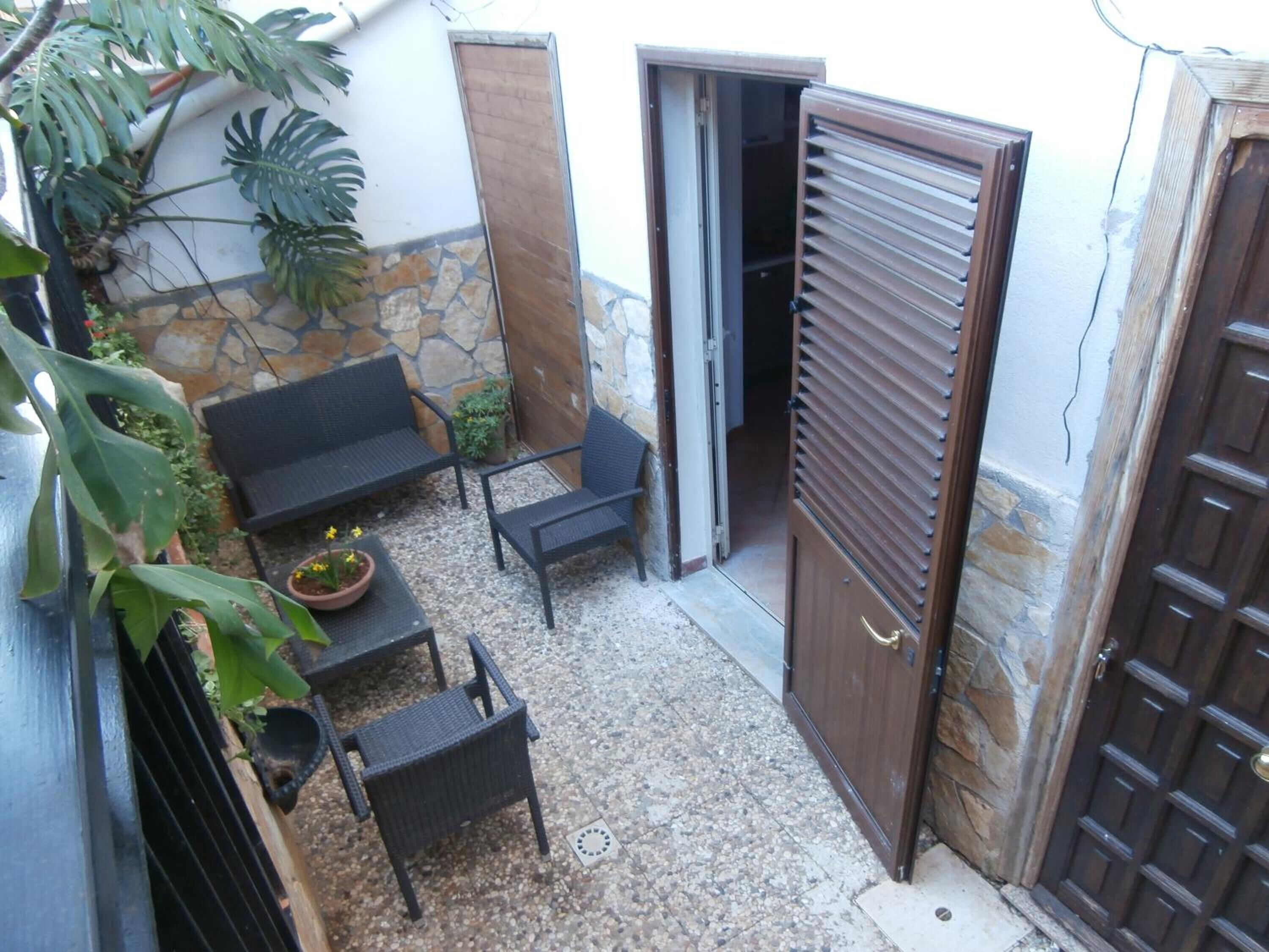 An outdoor patio with a stone wall, a wooden door, and a seating area with a table and chairs.