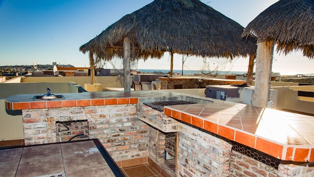 Un área de bar al aire libre con chimenea de ladrillo, una parrilla y un paraguas con techo de paja.