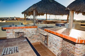 An outdoor bar area with a brick fireplace, a grill, and a thatched roof umbrella.