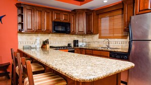 Una cocina con armarios de madera, encimera de granito, refrigerador de acero inoxidable y microondas integrado.