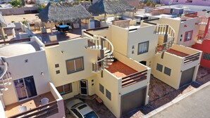 Un edificio residencial de varios pisos con un coche estacionado en la planta baja, una escalera y un balcón con barandilla.