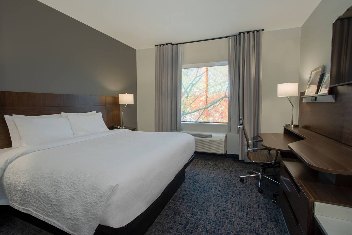 A hotel room with a large bed, a desk, two lamps, a chair, and a window with curtains.