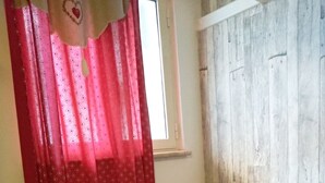A room with a wooden wall, a window with a white frame, and a bench with red cushions and heart patterns.