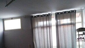 A room with two beds, a sofa, a window, and a curtain.