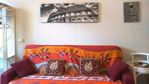 A room with a sofa adorned with colorful patterns, a wall-mounted picture of the Colosseum, and a metal object with text on the wall.