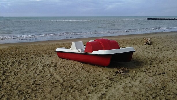 A red and white boat on a sandy beach with the ocean in the background.