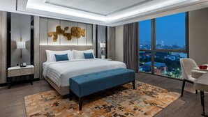 A modern hotel room with a large bed, a desk, and a view of the city at night. - Royal Malioboro Yogyakarta by Aston (Yogyakarta)