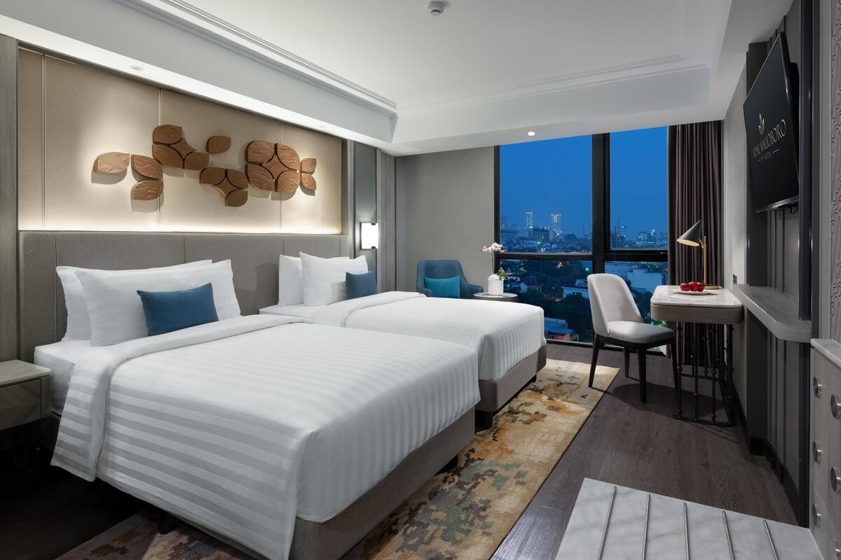 Ein modernes Hotelzimmer mit zwei Betten, einem Schreibtisch und einem großen Fenster mit Blick auf die Stadt.