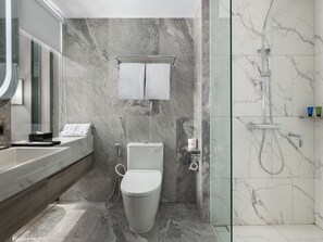 A modern bathroom with a marble floor, a glass shower enclosure, a toilet, and a vanity with a mirror. - Royal Malioboro Yogyakarta by Aston (Yogyakarta)