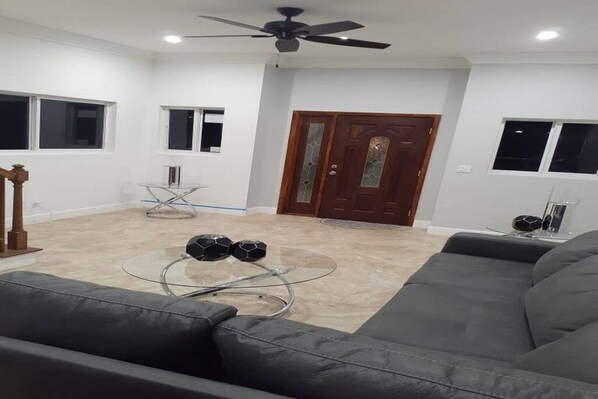 A living room with a sofa, a coffee table with two soccer balls, a glass table, and a wooden door.