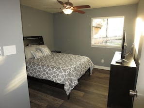 A bedroom with a bed, a ceiling fan, a window with blinds, a desk with a computer, and a door. - ASU Arizona State University Tempe Executive Condo (Tempe)