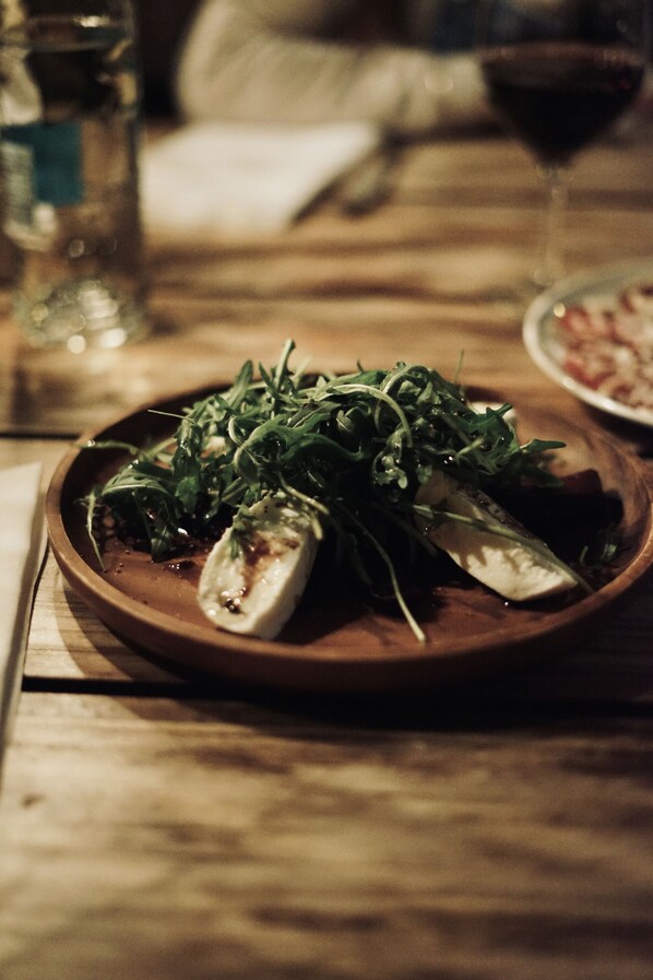 A wooden table with a plate of food, a glass of red wine, and a bottle of water. - L'Ovella Negra Mountain Lodge (Soldeu)