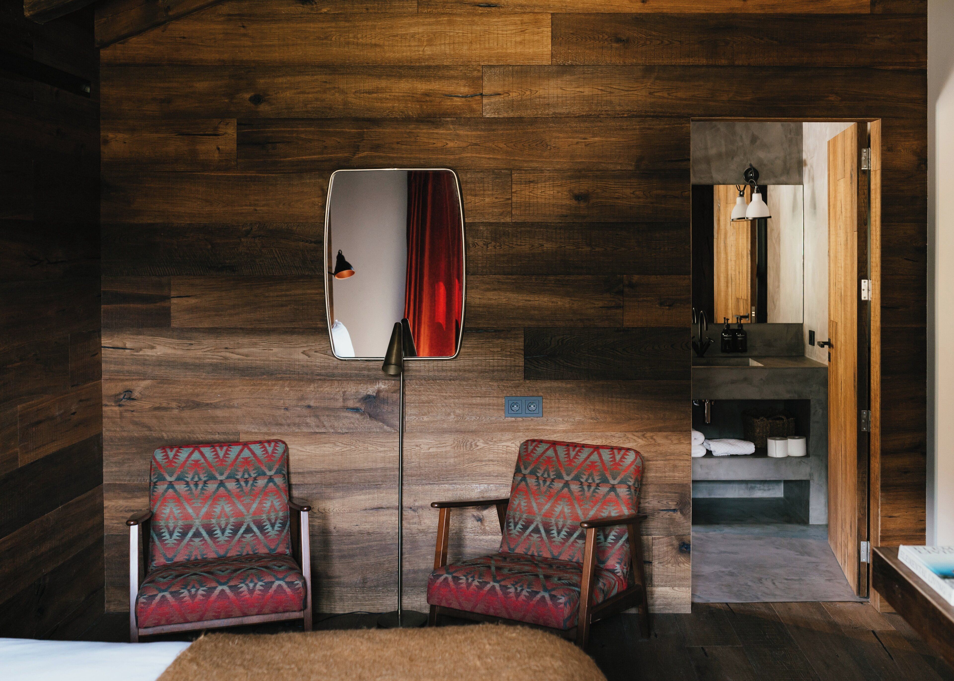 Ein Zimmer mit Holzwänden, zwei gemusterten Sesseln, einem Spiegel und einem kleinen Tisch.
