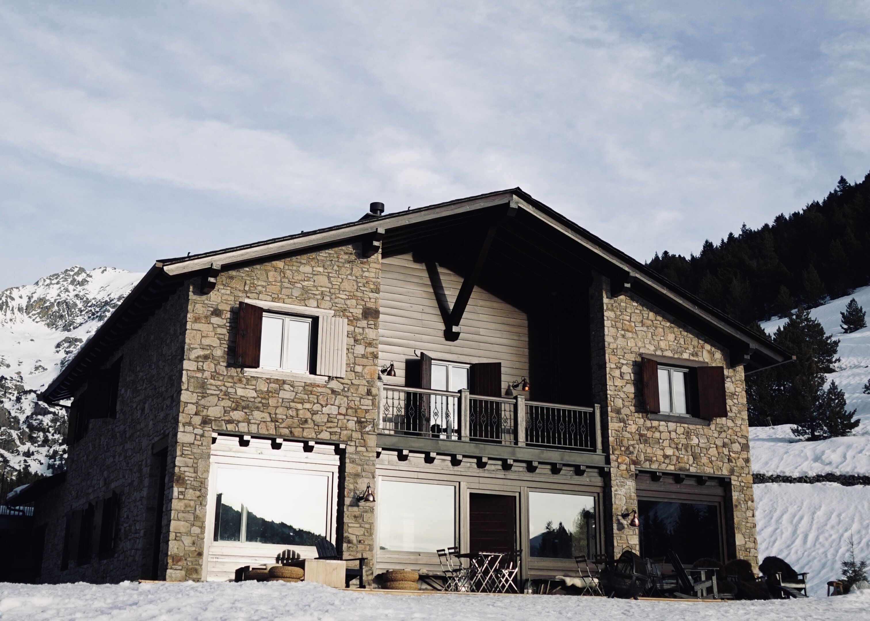 Een stenen huis met een balkon, grote ramen en uitzicht op besneeuwde bergen.