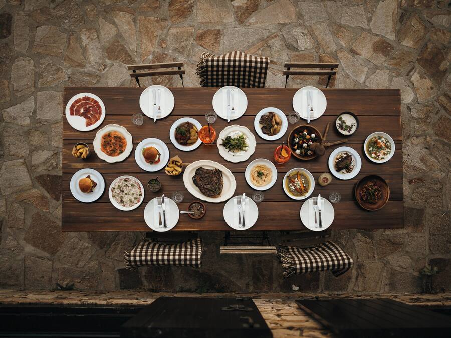 Una mesa de madera para comer dispuesta con diferentes platos y cubiertos frente a una pared de piedra.