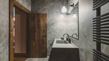Un baño con puerta de madera, lavamanos blanco y espejo con luces.