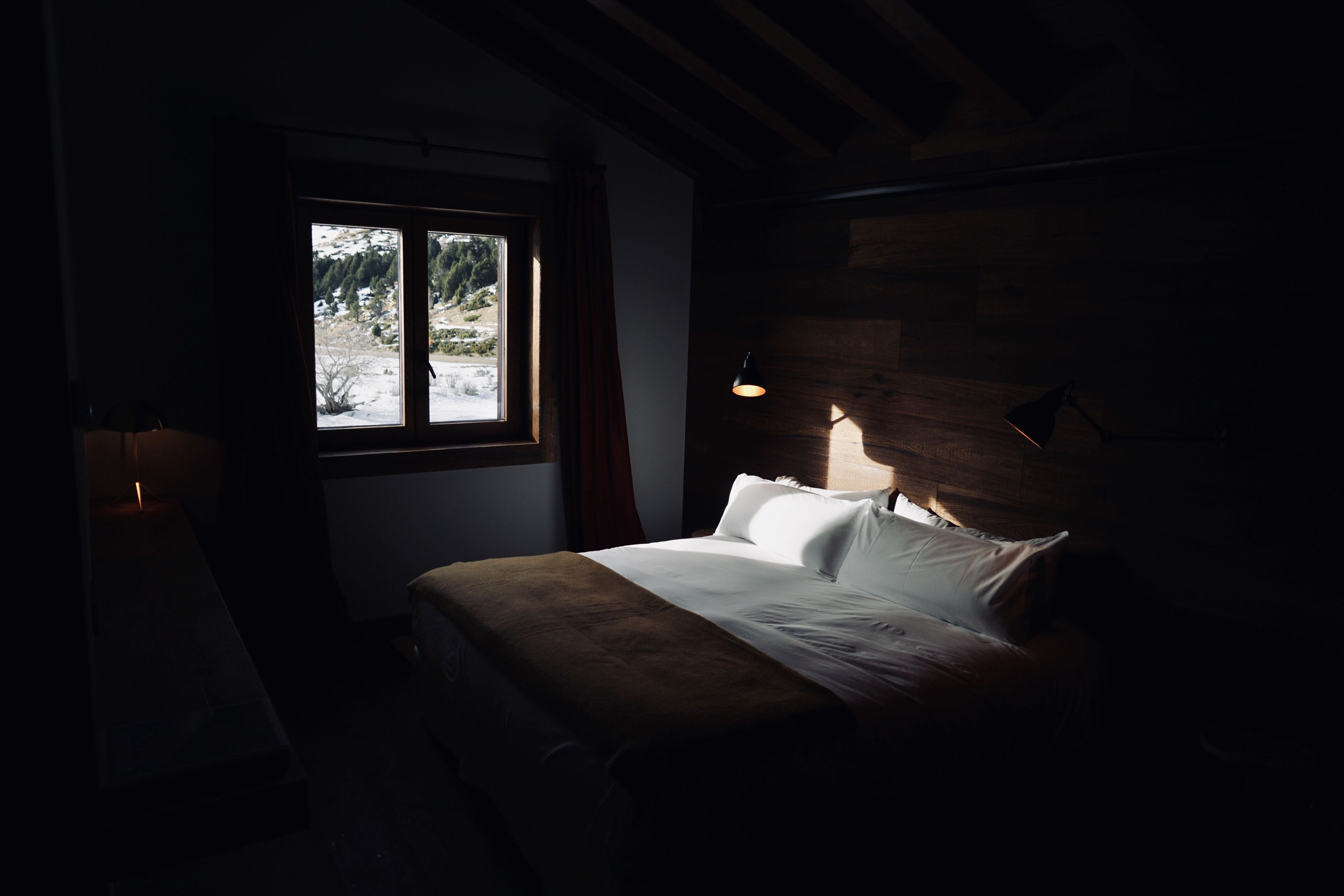 A dimly lit room with a bed, a window, and a wall-mounted lamp.