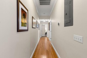 A hallway with framed pictures on the walls, a wooden floor, and a door on the right.