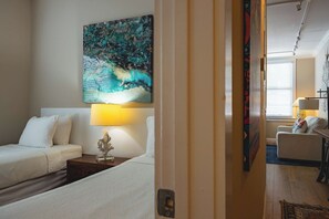 Une chambre d’hôtel avec un lit, une table de chevet, une lampe, un tableau et une vue sur une autre chambre.
