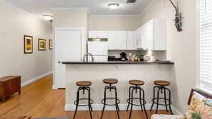 A kitchen with white cabinets, a black countertop, and four stools. - The Mesa House - One block from Duval St (Key West)