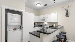 A compact kitchen with white cabinets, a microwave, a stove, and a small island with bar stools. - The Mesa House - One block from Duval St (Key West)