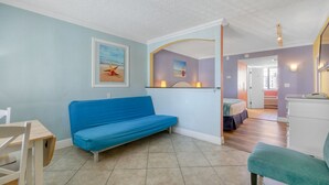 Ein Zimmer mit einem blauen Sofa, einem Holztisch und einem Bett mit blauer Bettdecke.