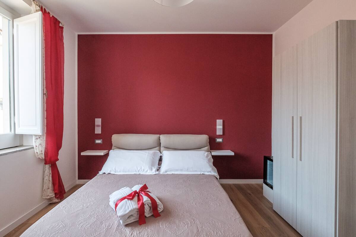 Une chambre d’hôtel avec un mur d’accent rouge, un lit avec du linge de lit blanc, deux tables de chevet et une armoire.