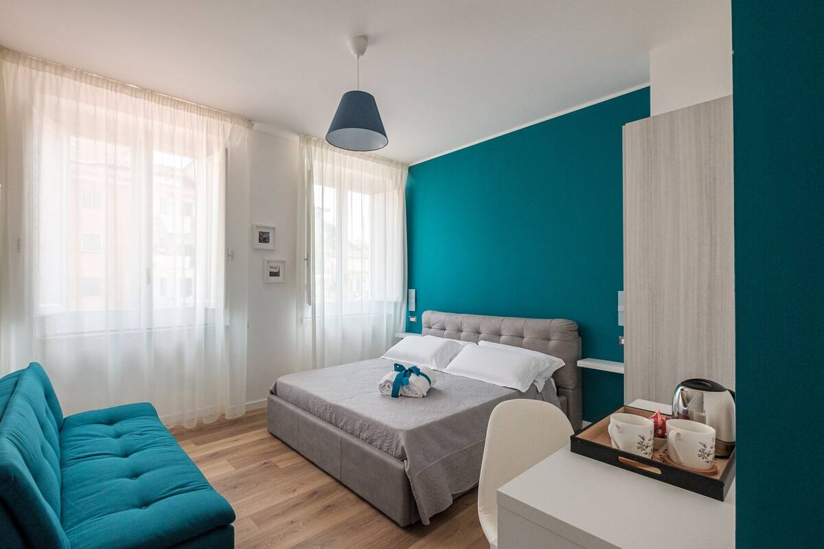 Une chambre d’hôtel moderne équipée d’un lit, d’un canapé, d’un bureau et d’une fenêtre avec des rideaux légers.
