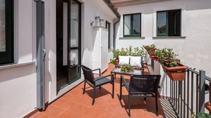 Un pequeño patio con una mesa y sillas, rodeado de plantas en macetas y una barandilla.