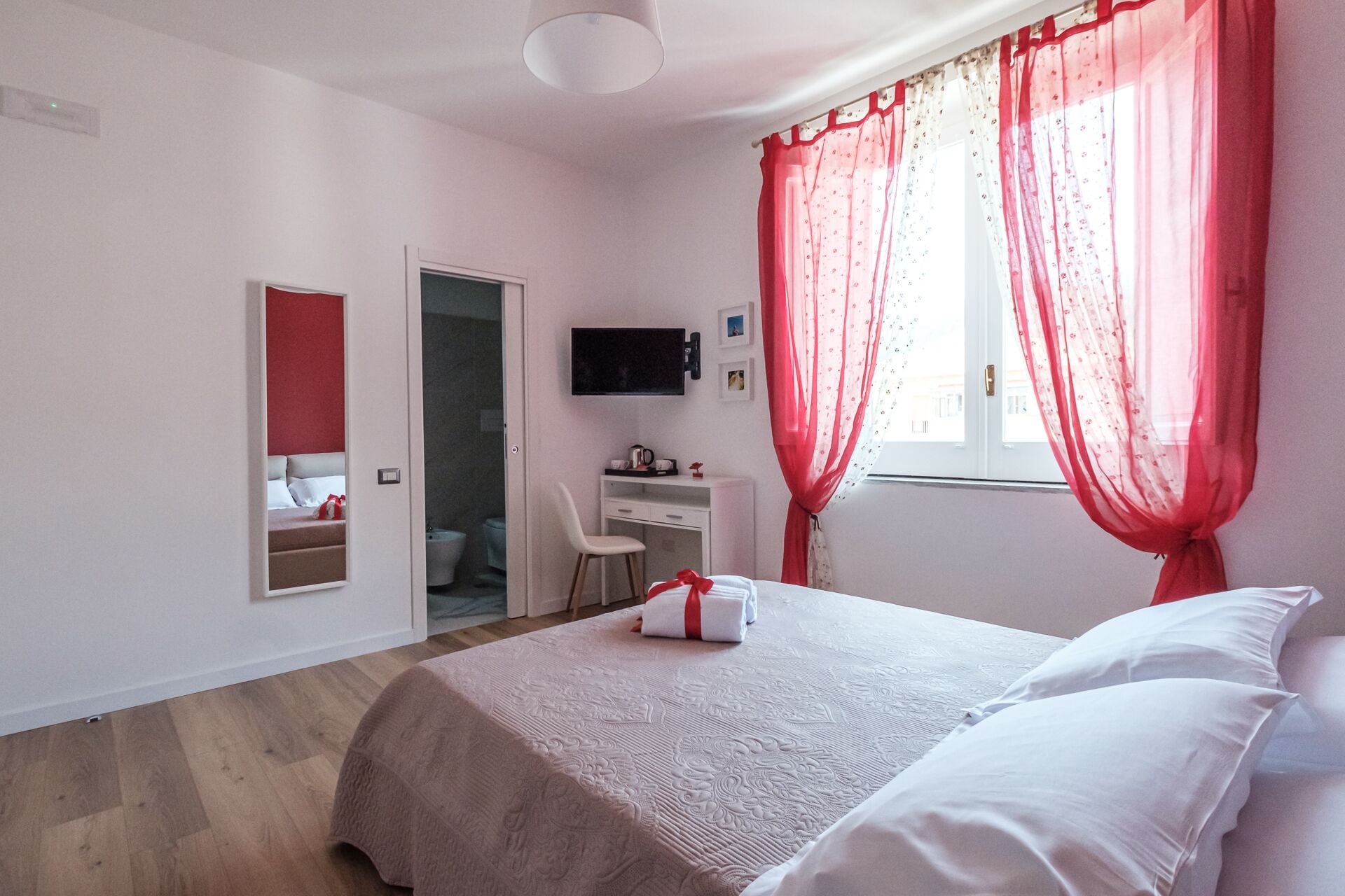Een slaapkamer met een bed, een bureau, een stoel, een televisie en een badkamer die door een open deur zichtbaar is.