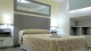 A neatly made bed with a patterned bedspread, a bedside lamp, a small table with a phone and a lamp, and a mirror above the bed. - Gran Hotel Laserre (Río Grande)