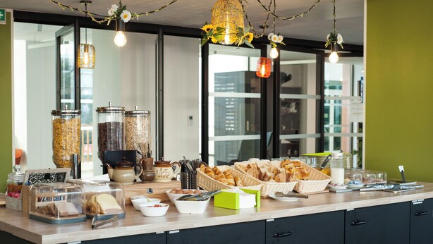 A breakfast buffet with various food items, baskets, and containers on a counter. - Moov'Appart Hotel Clichy (Clichy)