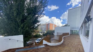 A rooftop terrace with wooden flooring, a curved railing, and a view of a parking area and buildings in the background. - Moov'Appart Hotel Clichy (Clichy)