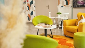 A modern living room with a green chair, a yellow sofa, and a small table with pastries. - Moov'Appart Hotel Clichy (Clichy)