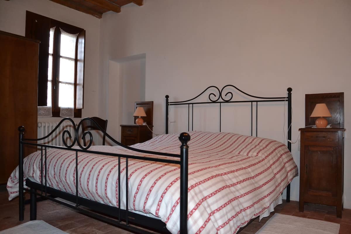 A bedroom with a bed, wooden wardrobe, and a nightstand with a lamp.