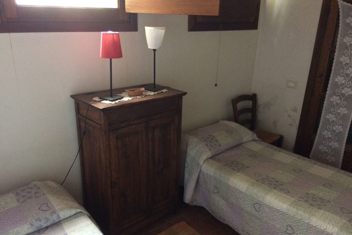 A small, dimly lit room with two single beds, a wooden cabinet, and two floor lamps.