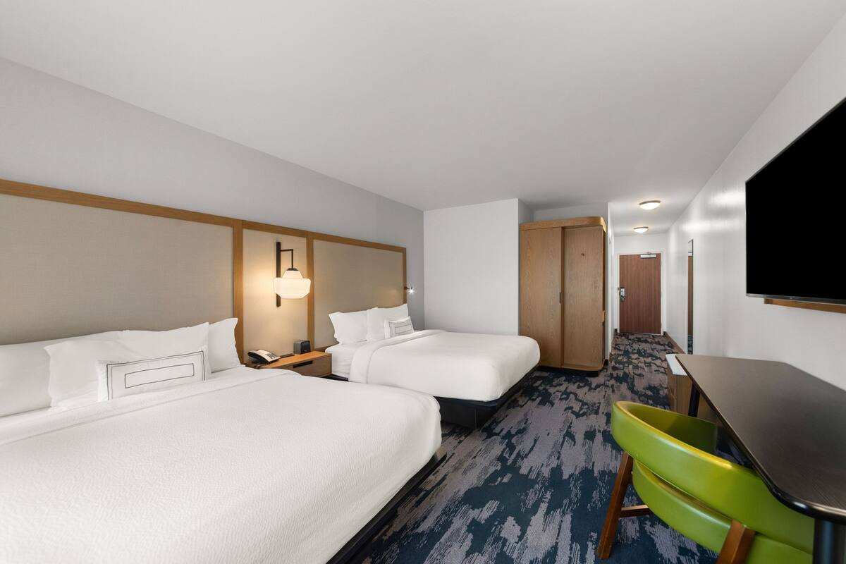 A hotel room with two beds, a desk, a television, and a bathroom door.