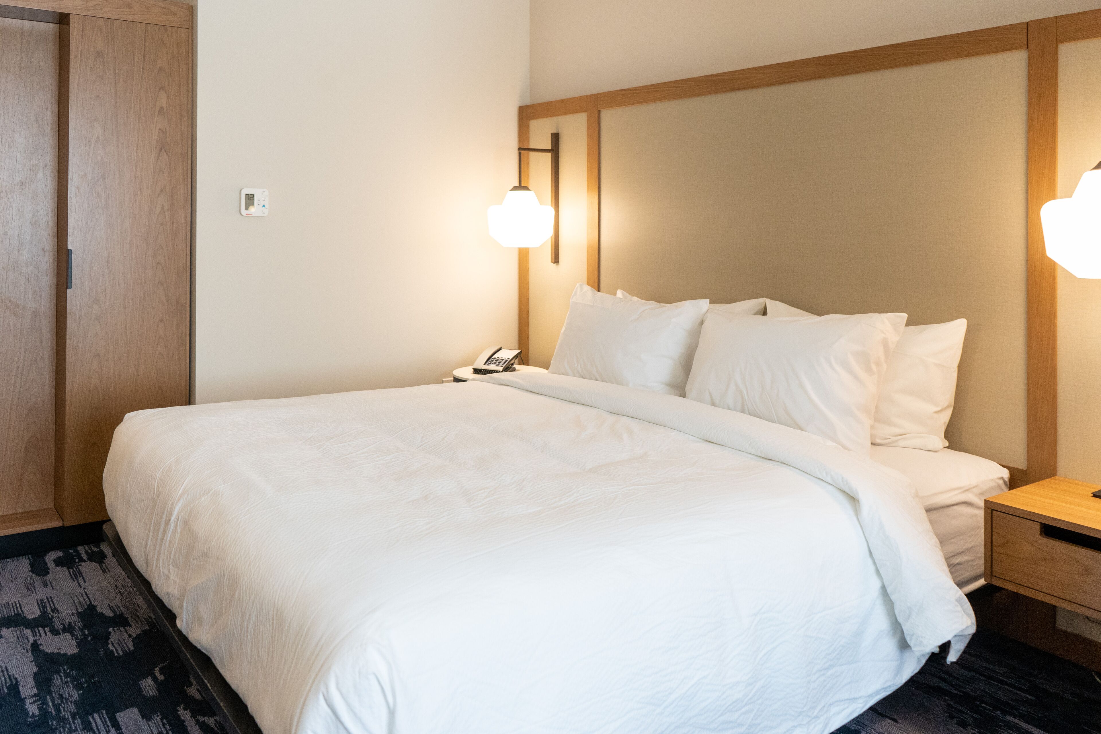 A hotel room with a large bed, bedside tables, a wooden wardrobe, and wall-mounted lighting.
